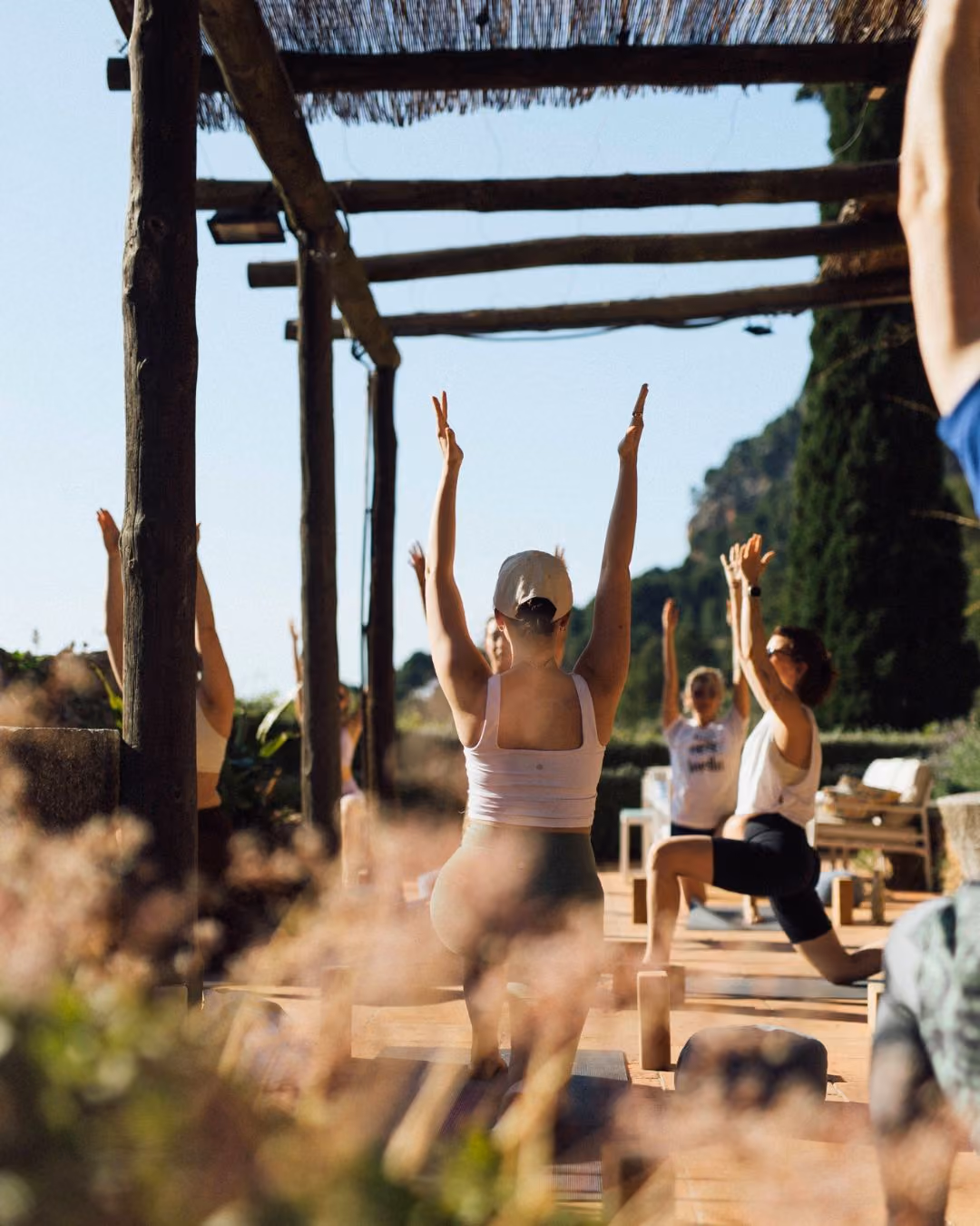 Group of people doing yoga stretches on the terrace at Finca Higo, Mallorca, under a wooden pergola with raised arms.