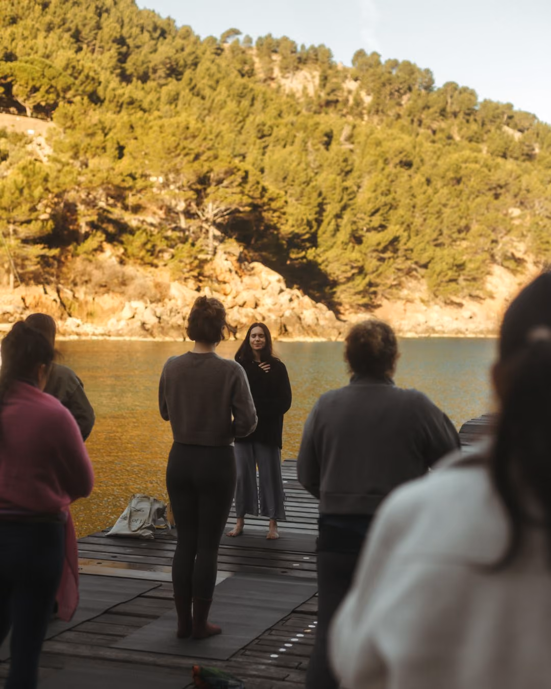 Group practicing yoga outdoors on a wooden dock on the coast of Mallorca at Finca Higo.