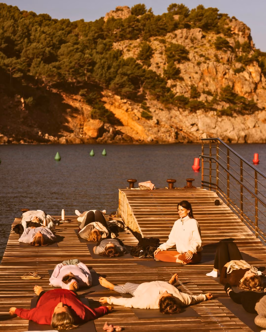 Group practicing yoga on a wooden dock by calm water at Finca Higo, Cala Tuent, Mallorca.