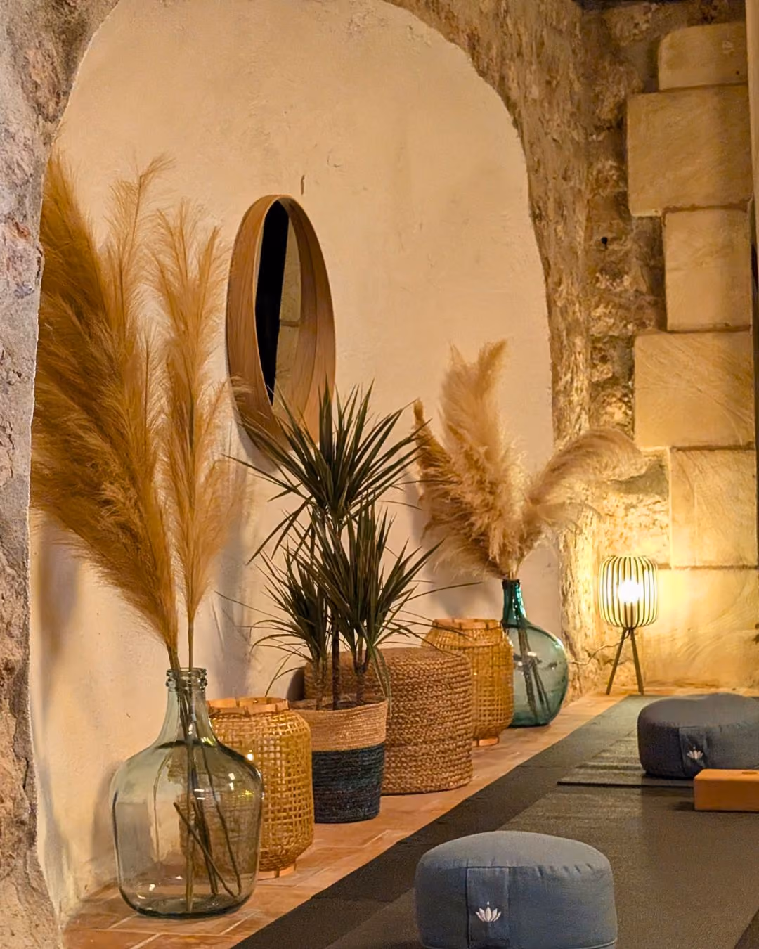 Cozy indoor yoga studio at Finca Higo, Mallorca, with wicker baskets, glass vases holding pampas grass, a small plant, and meditation cushions.