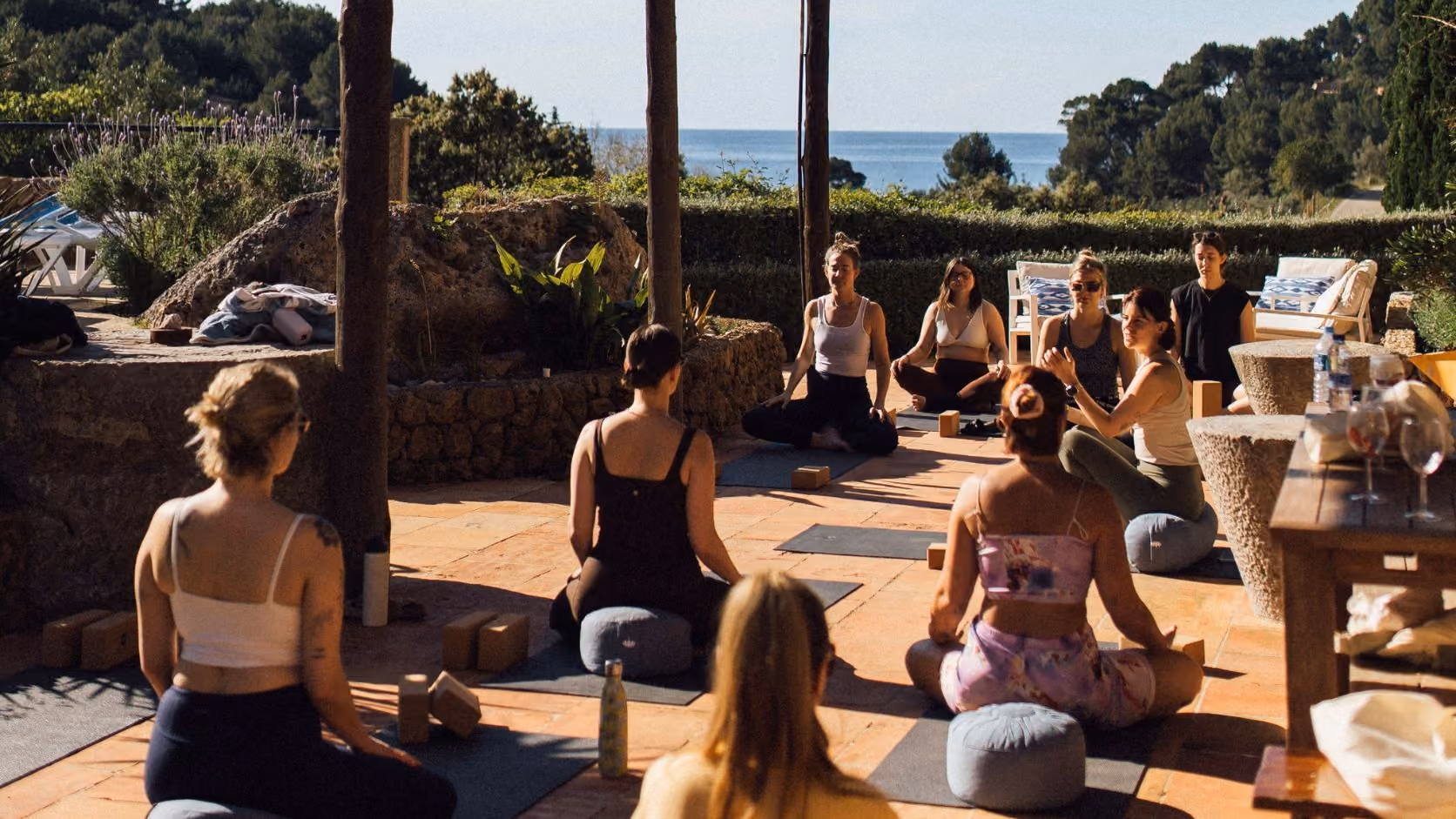 Group of women practicing outdoor yoga with meditation cushions and ocean view in the background, Finca Higo, Mallorca.