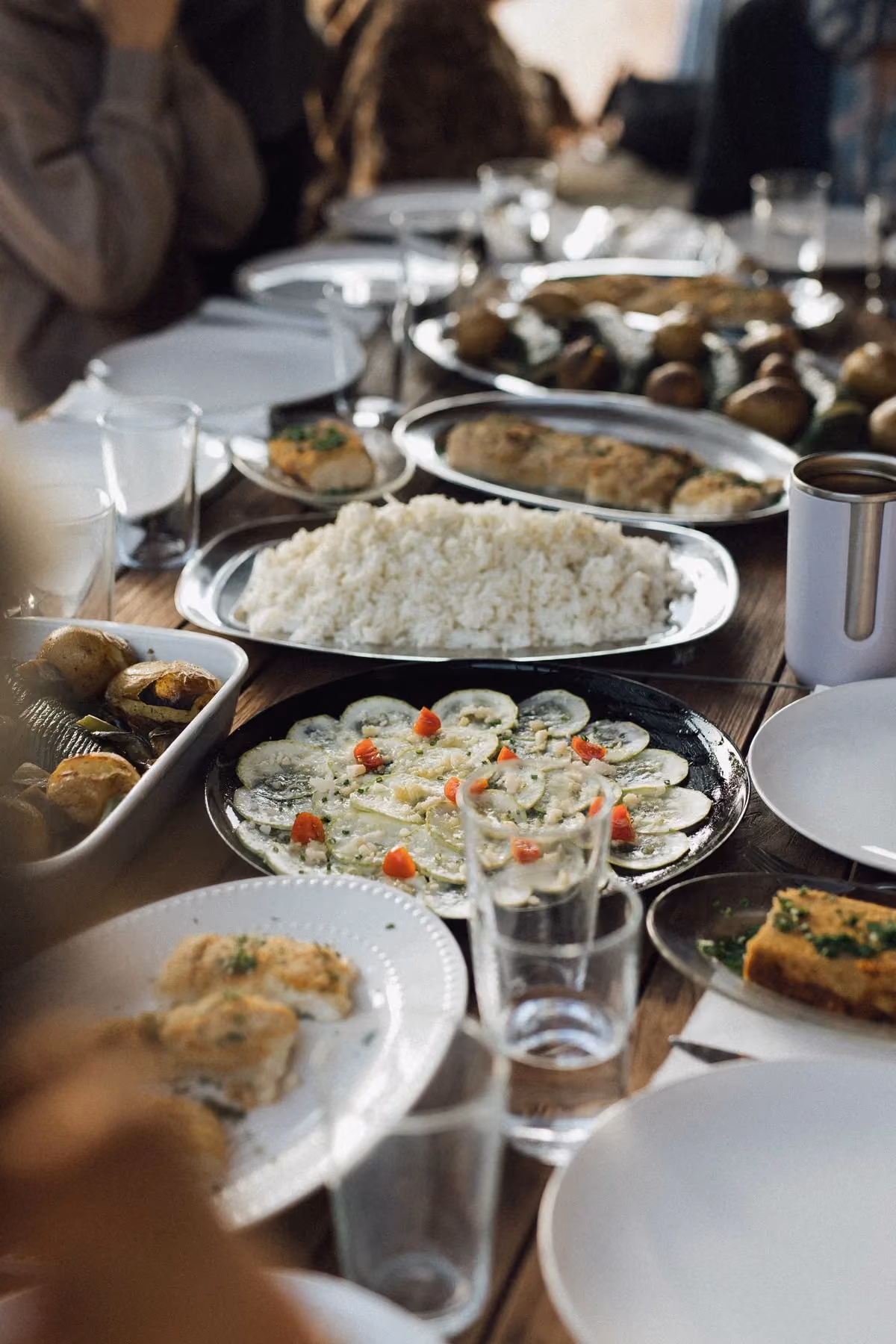 Table set with plates of food including rice, sliced cucumber salad, and roasted potatoes, created by our private chef Fernanda, Finca Higo, Mallorca.