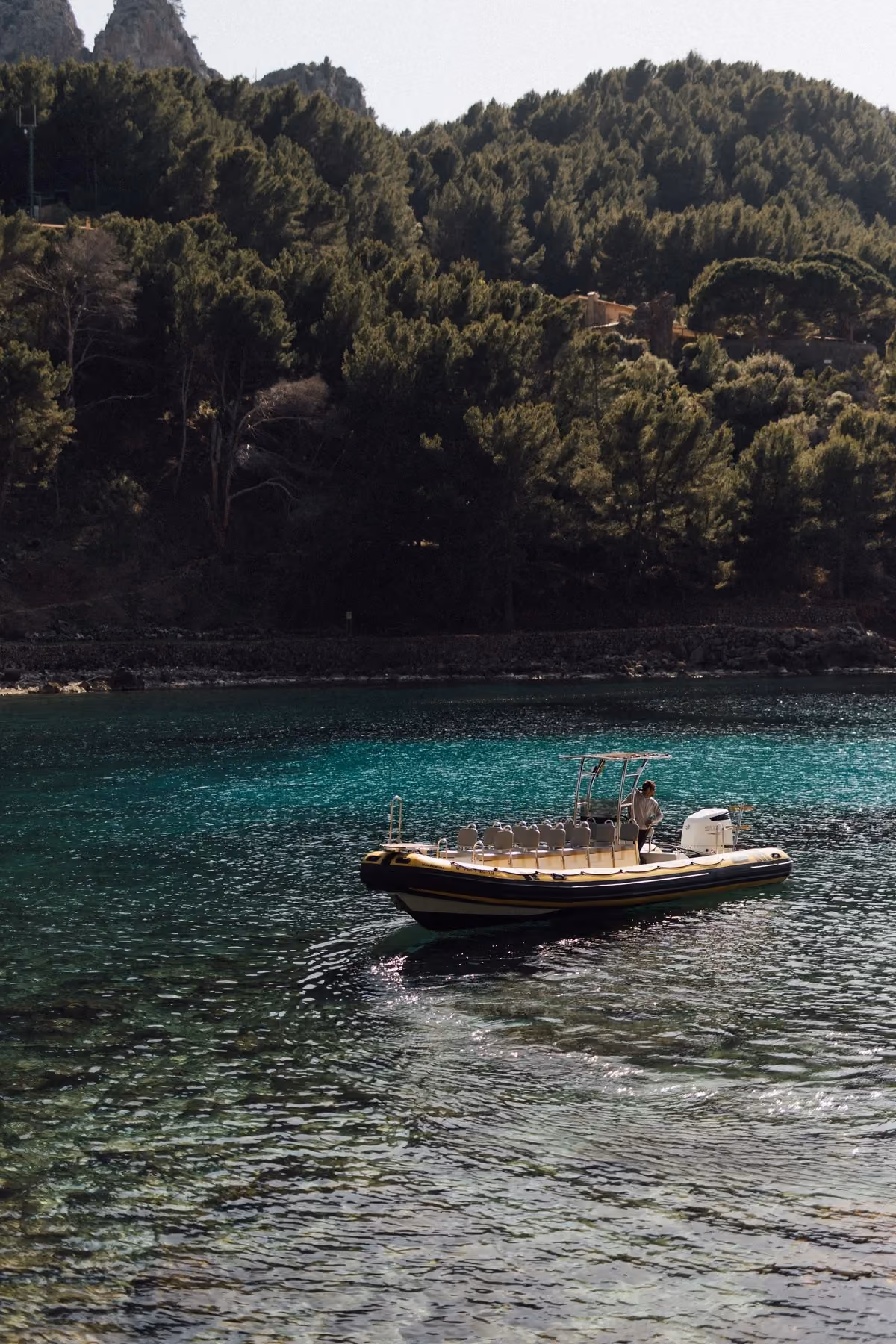 Small motorboat with seats floating on clear water near a forested shoreline, Mallorca.