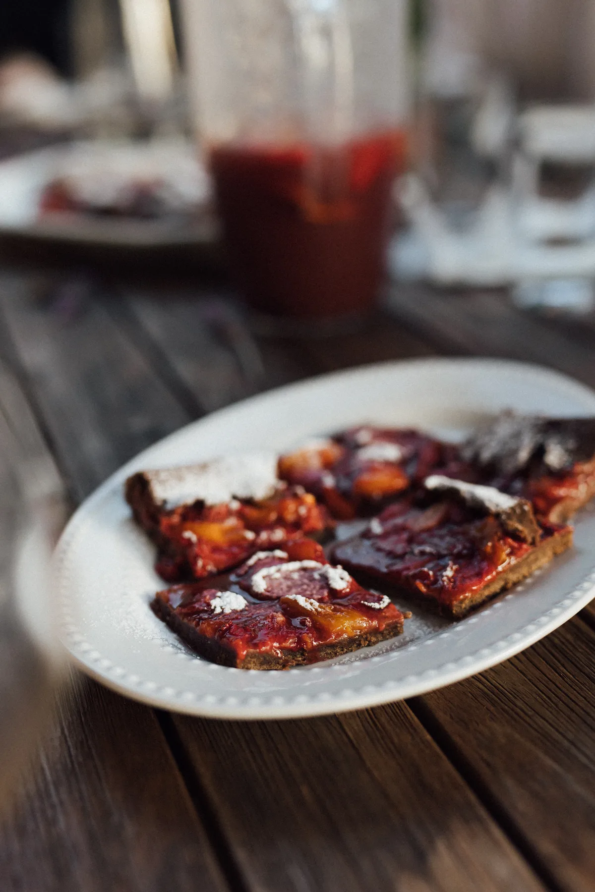 Slices of fruit tart with red and orange topping on a white plate on a wooden table, Castello Higo, Tuscany.