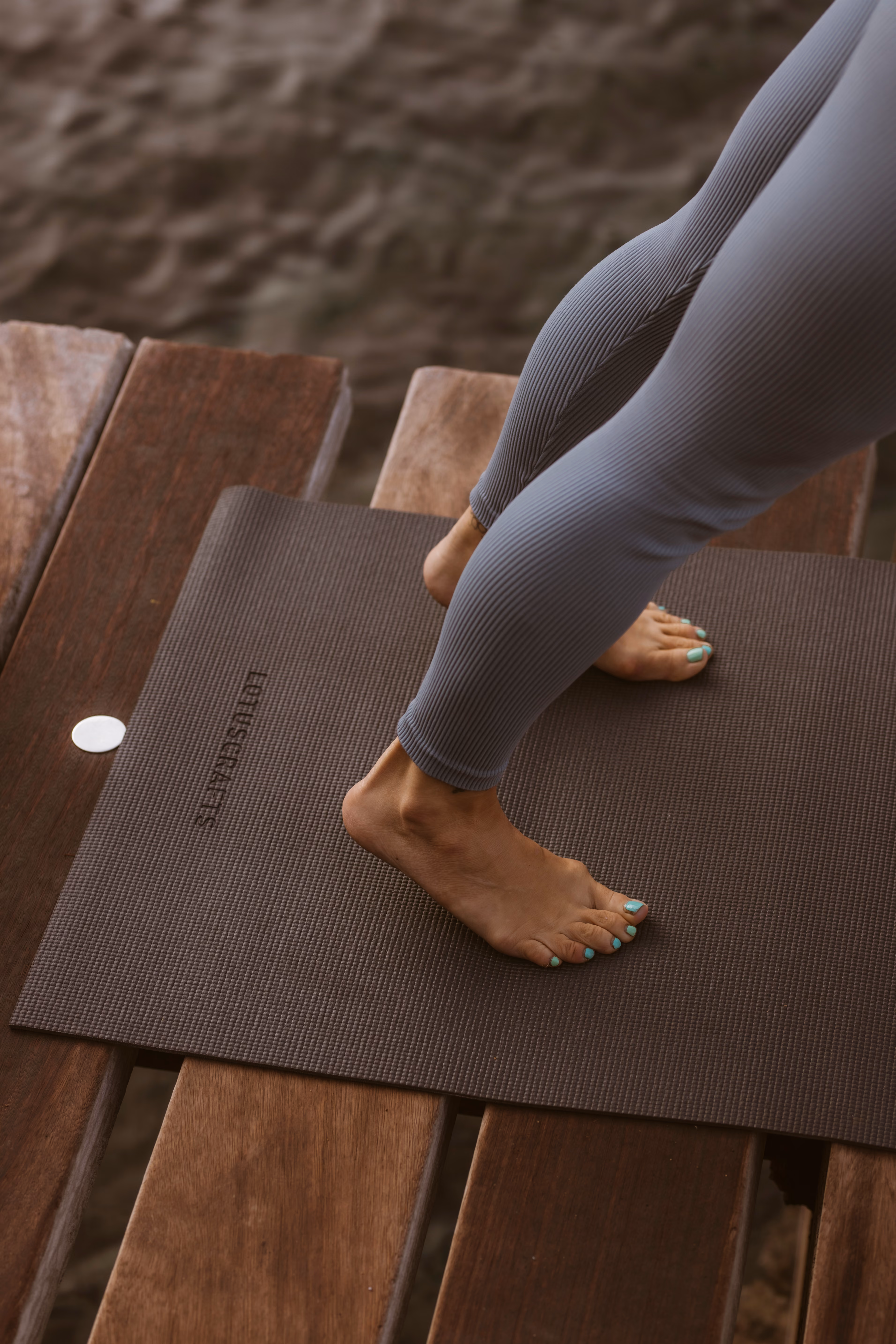 Bare feet with teal nail polish on a brown yoga mat over wooden boards near water, Finca Higo, Mallorca.