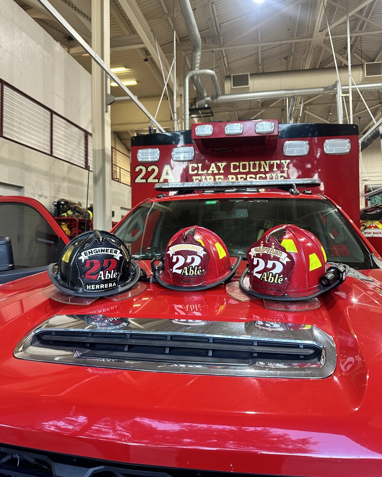 Three firefighter helmets labeled Engineer, Lieutenant, Captain 22 Able on a red fire rescue vehicle.