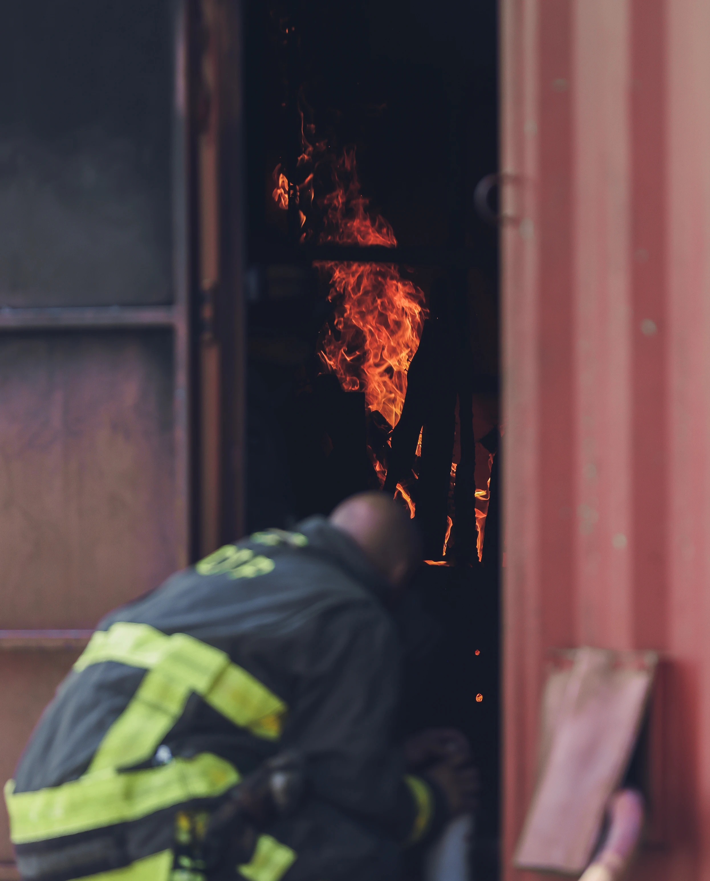 Firefighter crouching near an open door with visible flames inside a building.