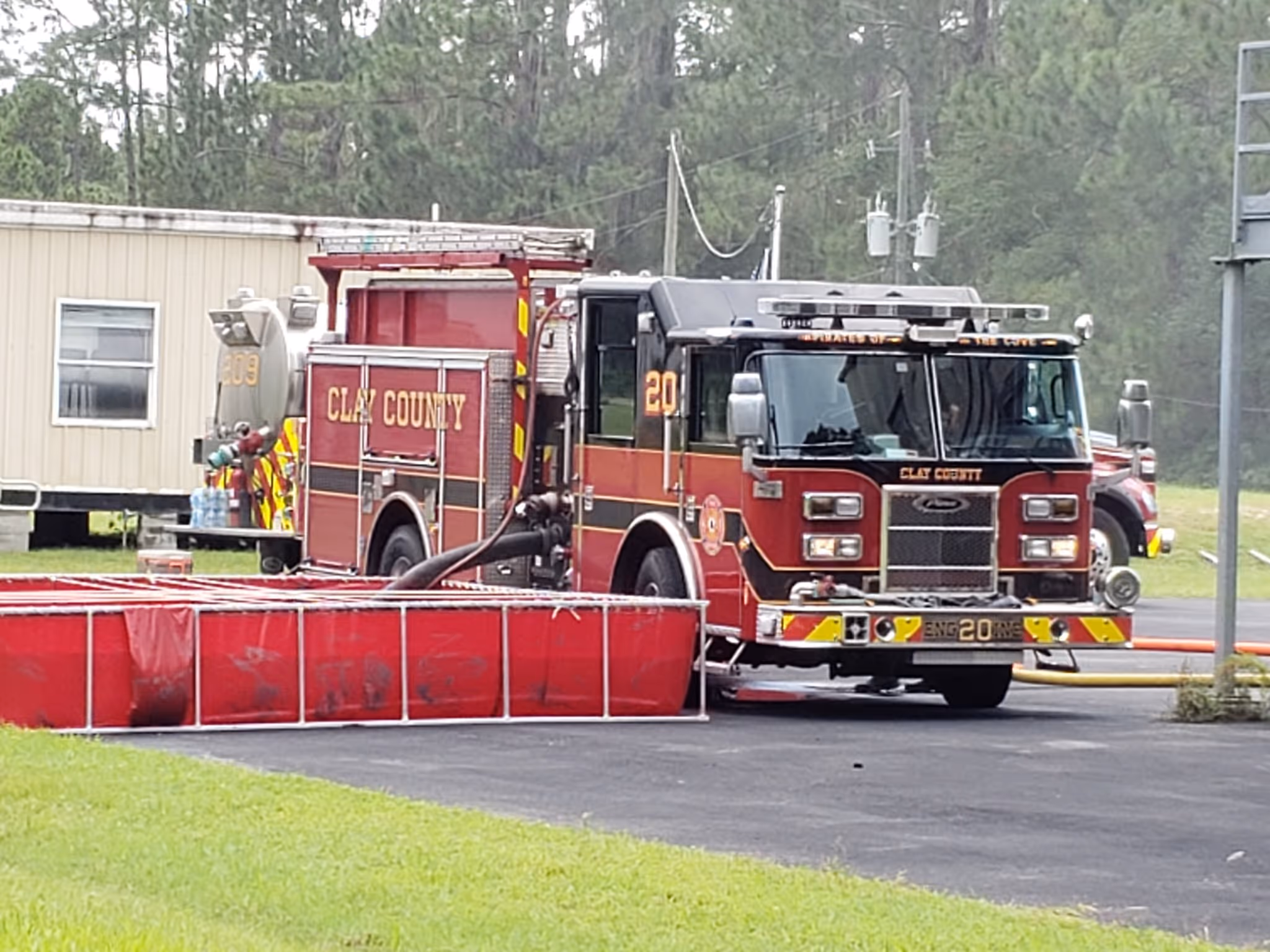 Red Clay County fire truck by a portable tank filled with water on a paved surface near a beige building.