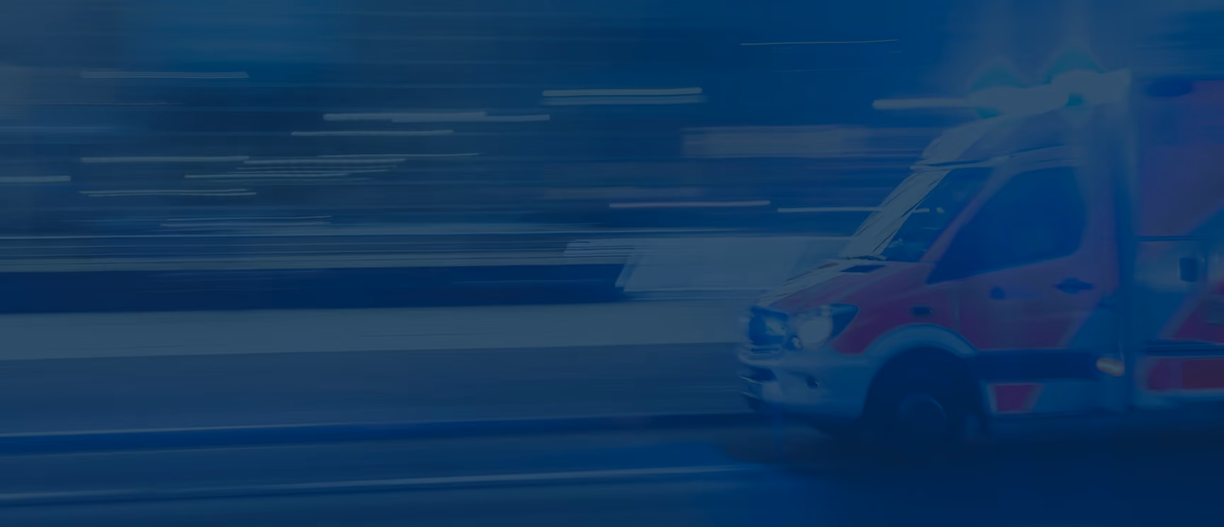 Blurred image of a red ambulance with flashing lights moving quickly on a street.