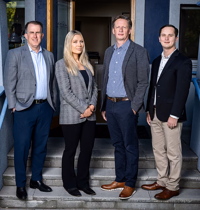 Four professionally dressed individuals standing on outdoor stairs in front of a building entrance, posing for a group photo.