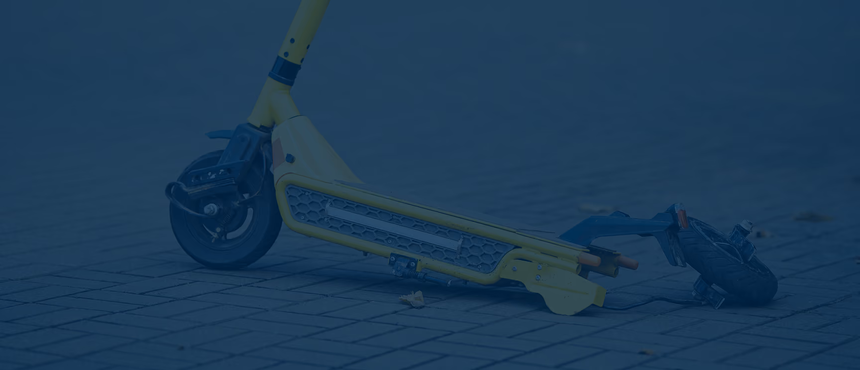 A yellow electric scooter lies broken on a tiled ground with its front wheel detached and the deck cracked.