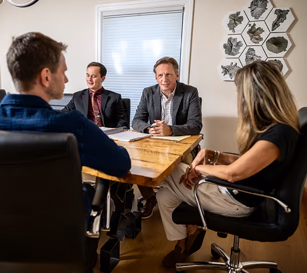 Four people having a business meeting around a wooden table in a brightly lit room with a window and decorative wall art.