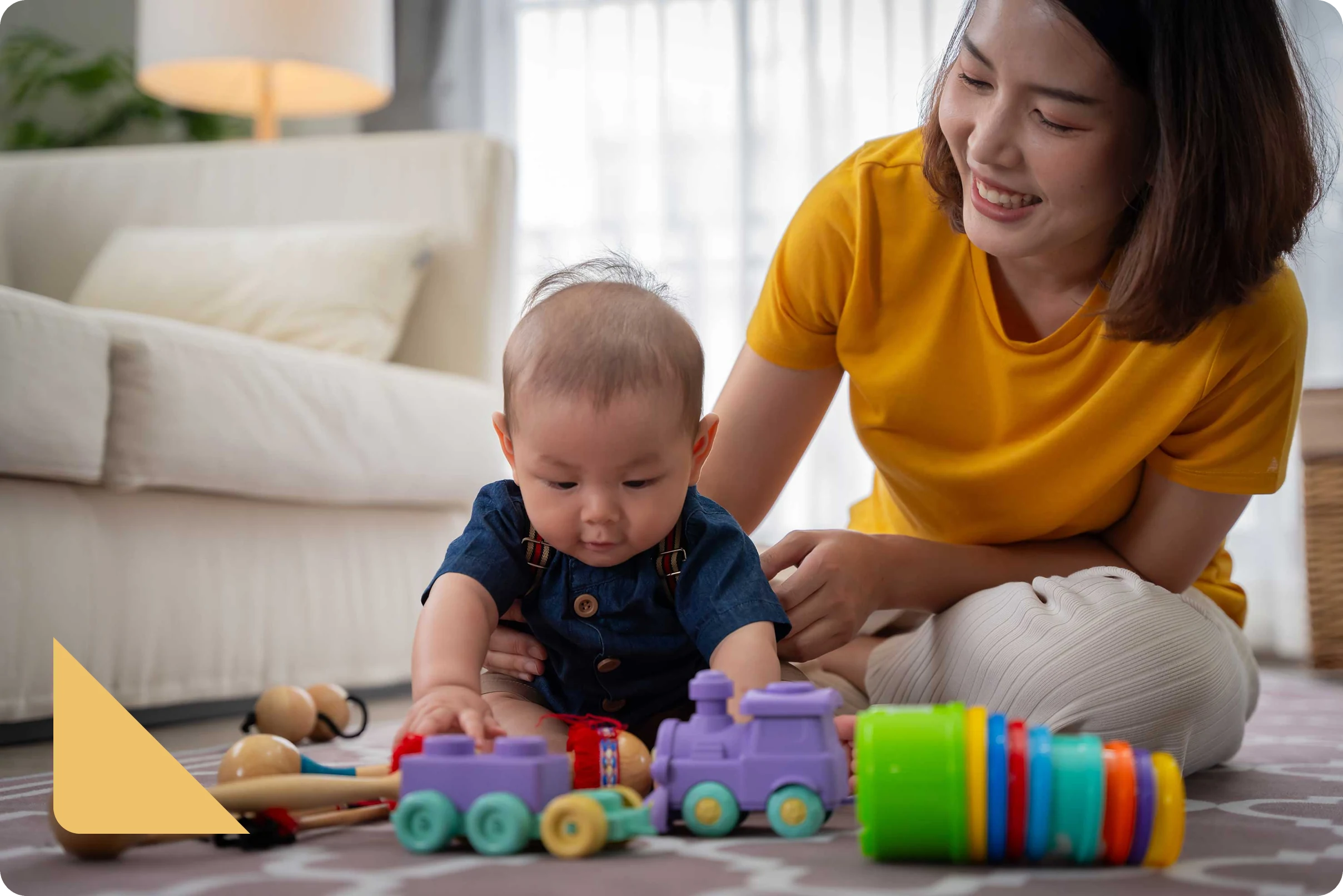 Smiling woman in yellow shirt watching a baby play with colorful toys on a carpeted floor