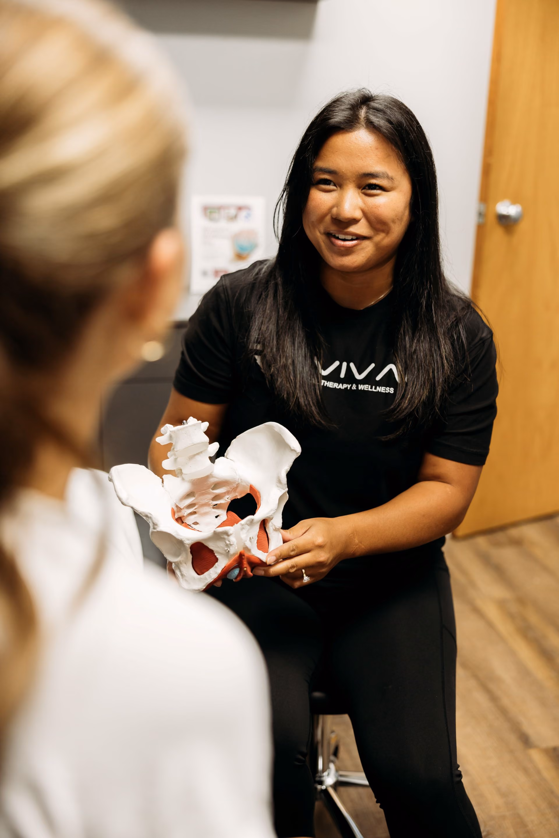 Physical therapist explaining a pelvic anatomy model to a patient during a consultation.