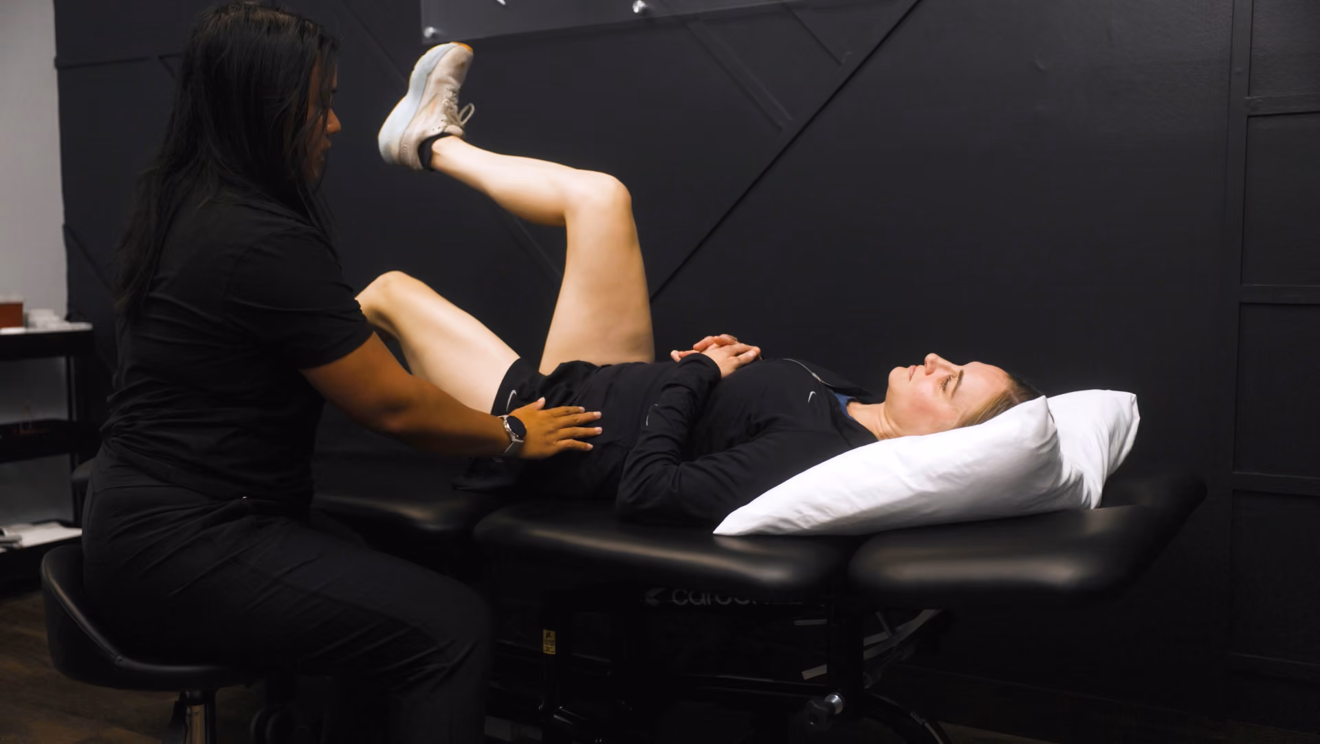 Physical therapist guiding a patient through a hip mobility exercise on a treatment table.