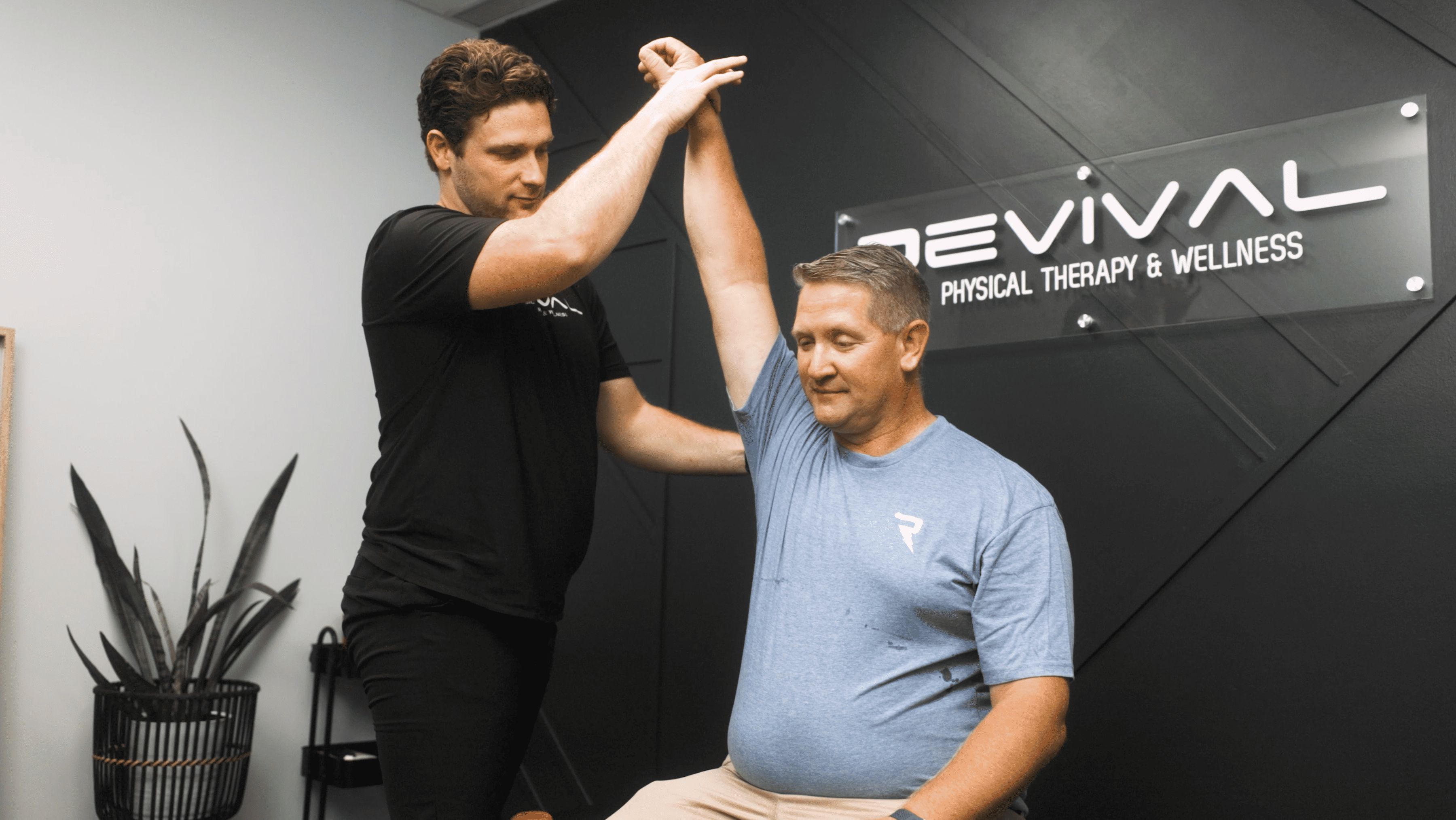 A Revival specialist performs manual therapy and arm stretching on a patient seated on a physical therapy table.
