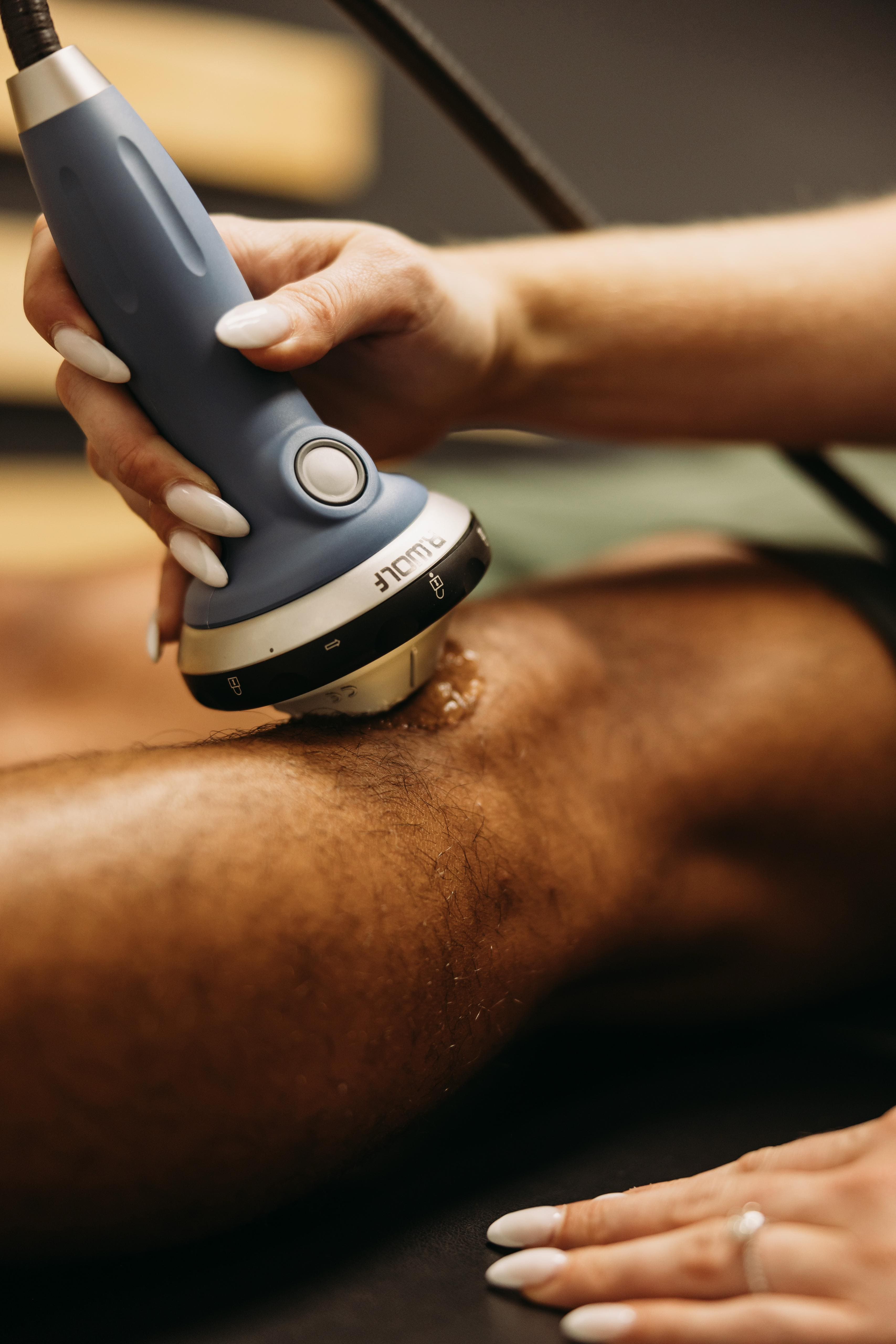 Physical therapist using a handheld shockwave therapy applicator on a patient's leg at Revival Physical Therapy & Wellness