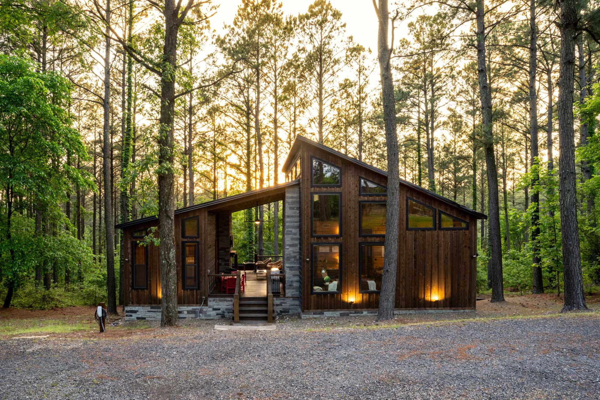 Showcasing a combination of stone and wood architecture, this cabin offers a welcoming entrance with its expansive porch and open design. Beautiful uplights and floodlights illuminate the exterior at night.