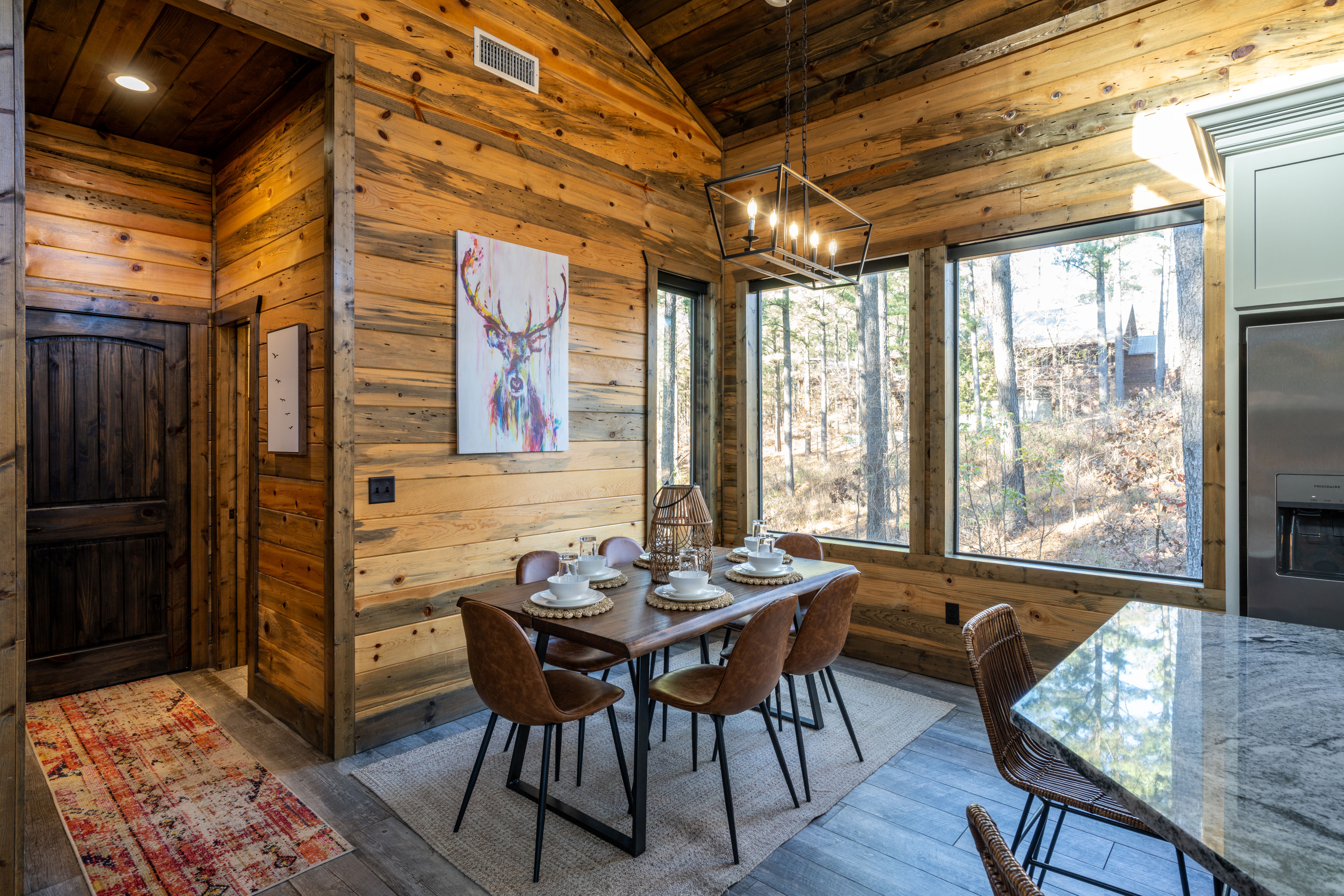 Enjoy meals in this dining area, featuring a modern wooden table, leather chairs, and views of the greenery through large windows.