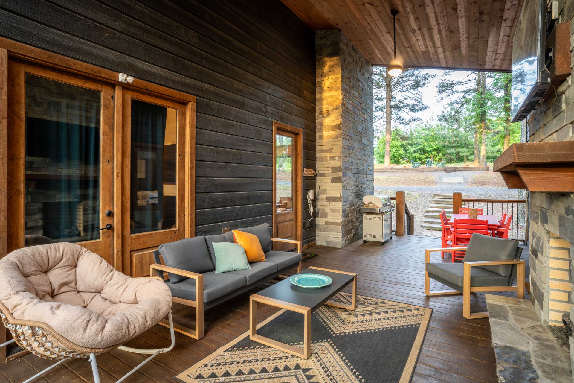 An outdoor lounge area complete with a modern fireplace, TV, comfortable seating and a 6-burner gas grill on a sheltered deck, perfect for gatherings in any weather. 