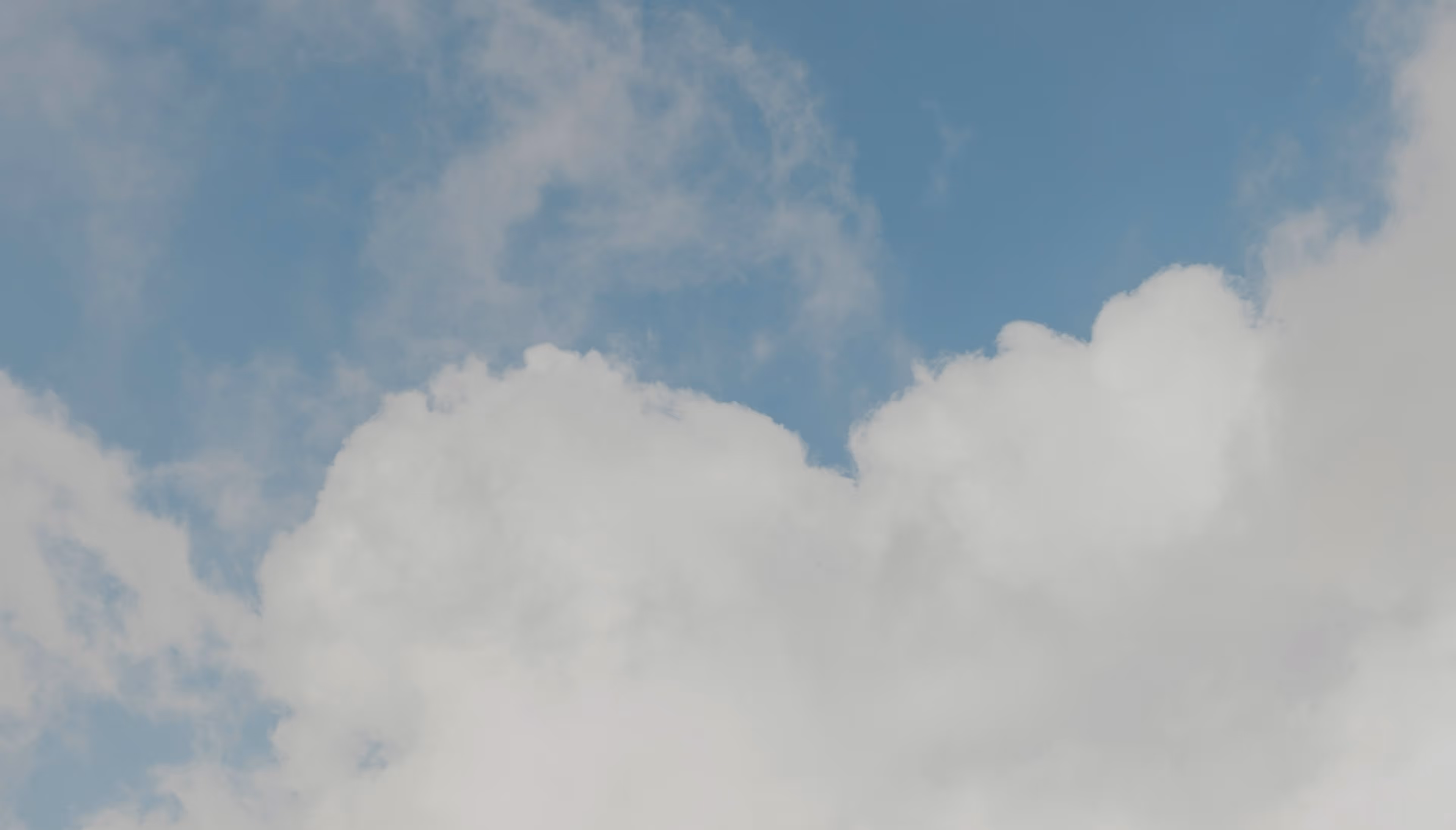 Blauer Himmel mit großen weißen Wolken unten und leichtem Harren darüber.