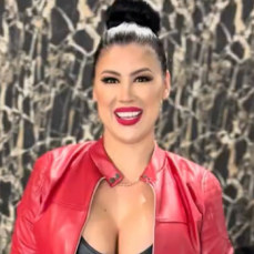 Woman with dark hair in a bun wearing a red jacket and bright red lipstick smiling.