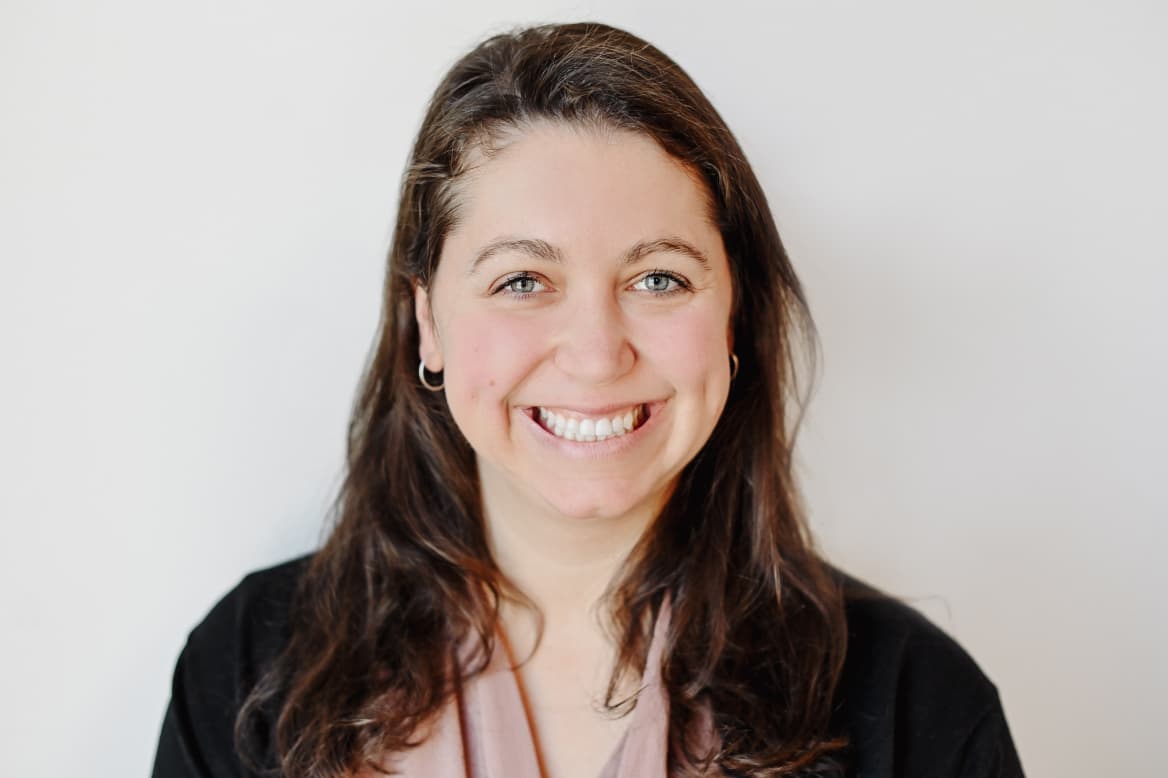 Worximity employee. Smiling woman with long brown hair wearing a black top and pink scarf on a white background.