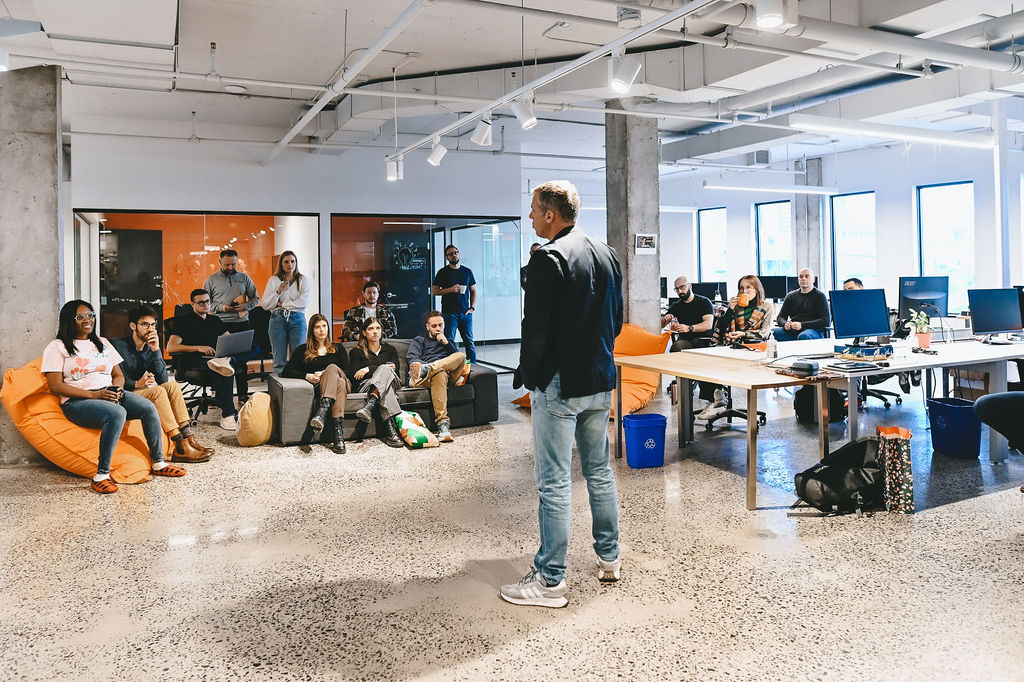 Man standing and speaking to a diverse group seated in a modern office space during a meeting.