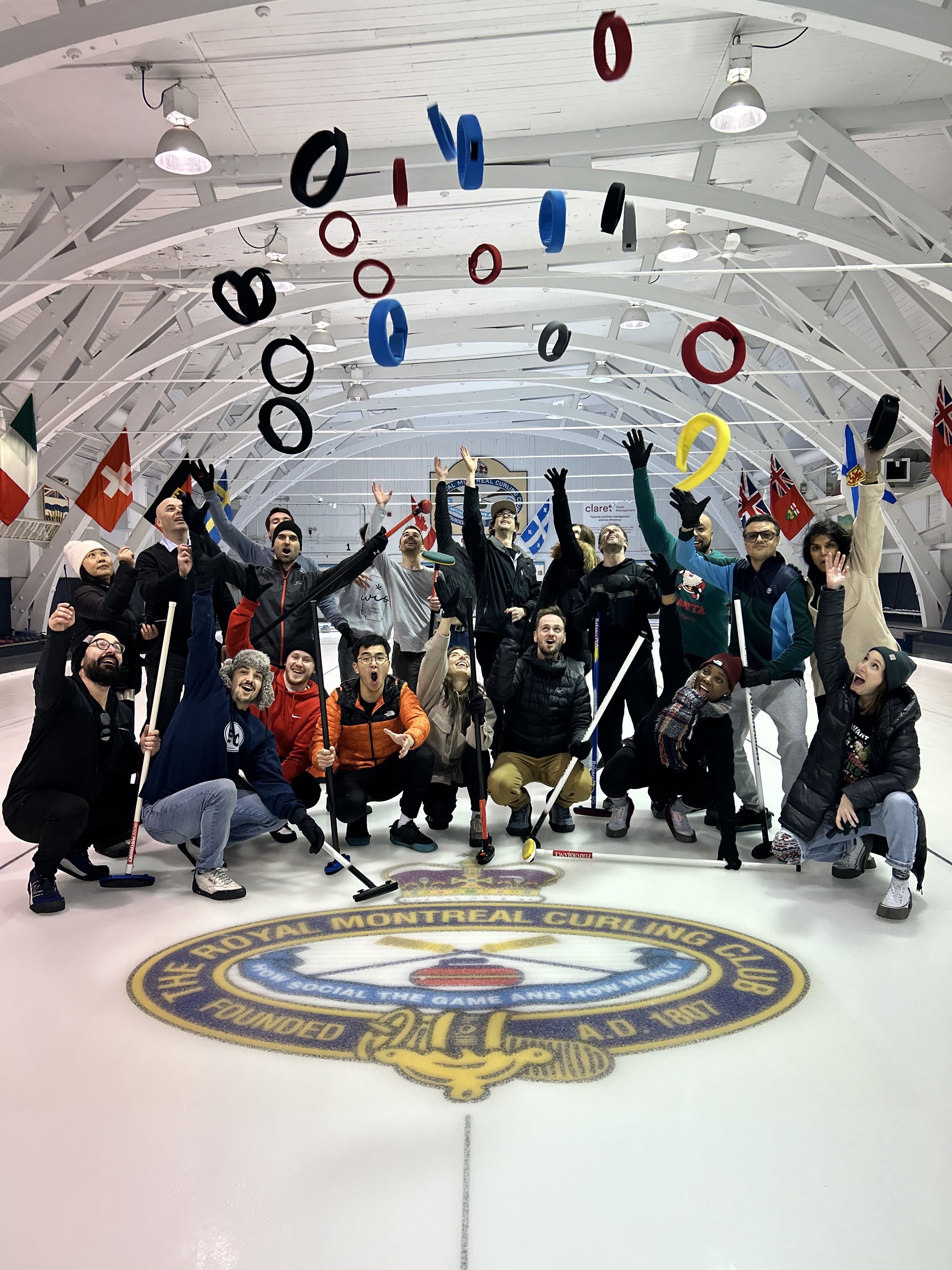 Group of curling players in a rink cheer as colored curling rings are tossed in the air above them.
