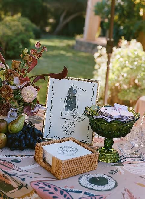 Table centerpiece with mixed flowers, pears, grapes, and lit candles in a cozy dining setting.