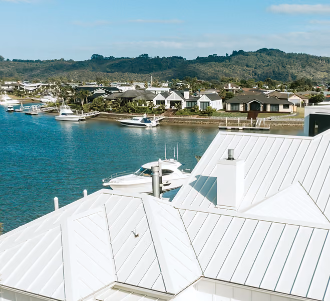 Waterfront neighborhood with boats docked by houses and white rooftops in the foreground under a clear sky.