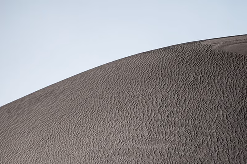 A close-up view of a large sand dune with fine ripples on its surface under a clear sky.