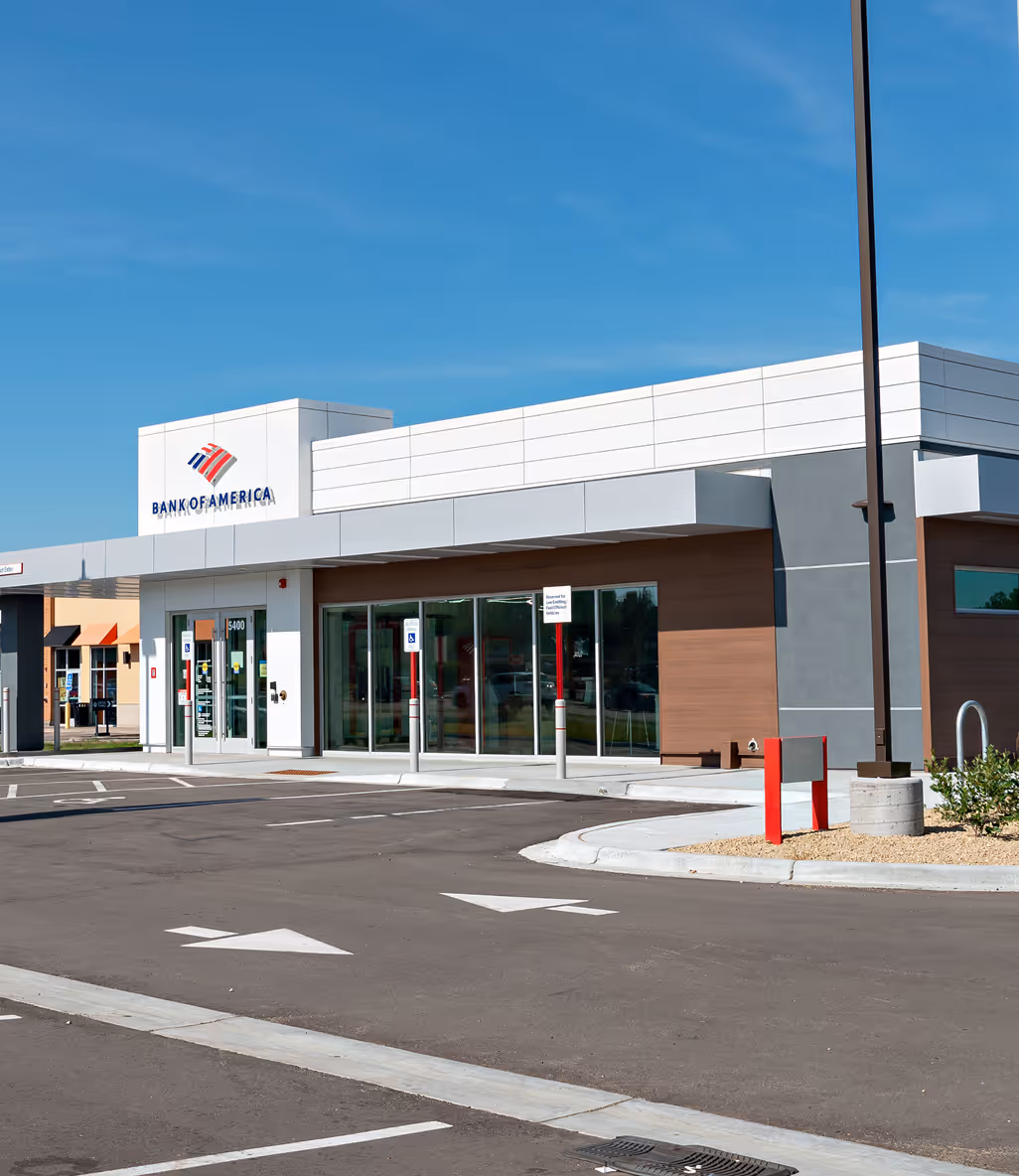 Modern Bank of America branch with glass doors, parking spaces, and blue sky.