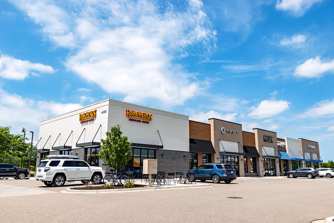 Strip mall with Pancheros Mexican Grill and other stores under a blue sky with scattered clouds.