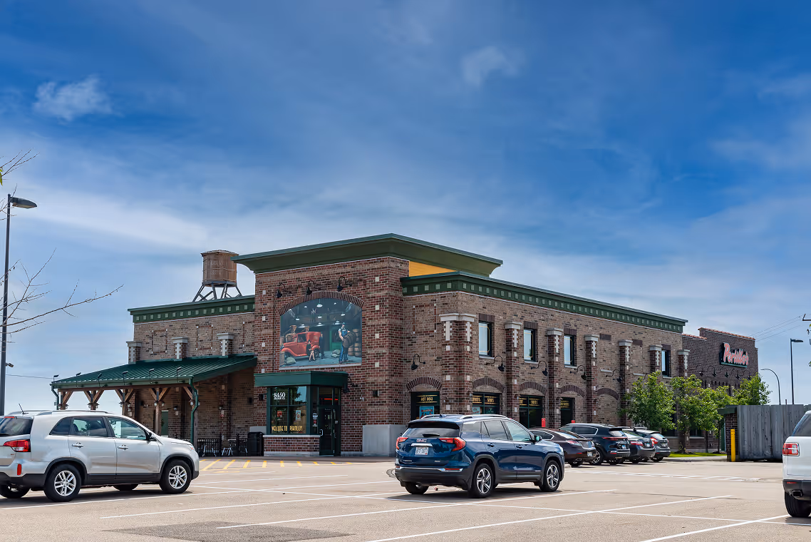 Brick restaurant building with green trim, mural of classic car, water tower, and parked cars under a blue sky.