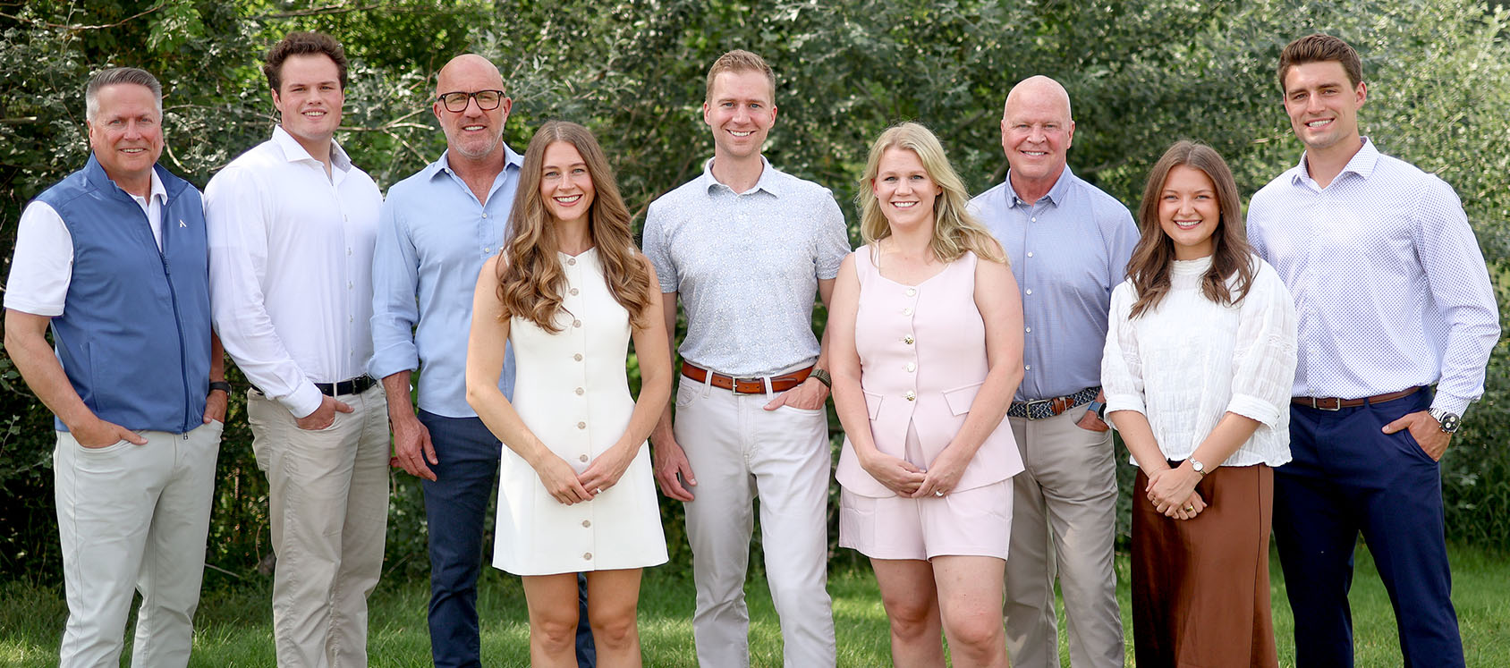 Group portrait of eight smiling people standing outdoors in casual and business casual attire.