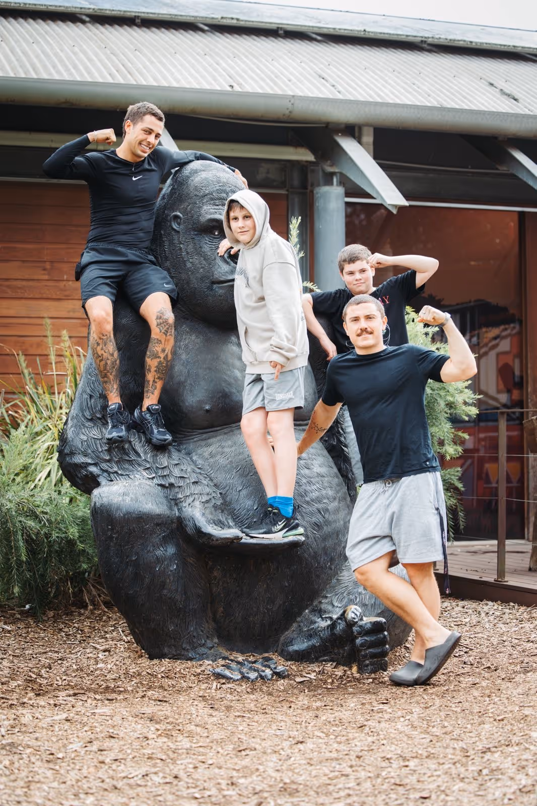 Four males posing and flexing muscles around a large black gorilla statue outdoors.