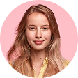 Smiling young woman with long blonde hair wearing a yellow shirt against a pink background.