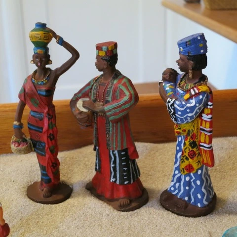 Three colorful figurines of African women in traditional attire, one carrying a pot, one with a drum, one holding a baby.
