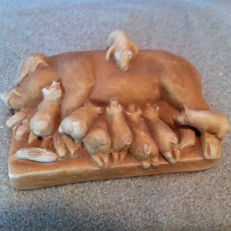 Brown ceramic sculpture of a dog lying with puppies nursing and one puppy on its back.