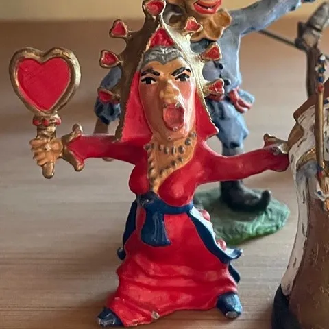Figurine of a woman in a red dress holding a heart-shaped mirror with a dramatic facial expression.