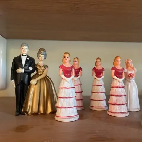 Ceramic wedding cake toppers with a groom, bride in gold dress, and bridesmaids in white with red details.