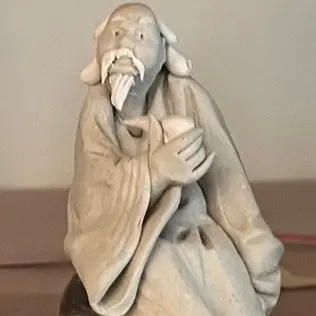 Sculpture of an elderly man with a long beard, holding a cup while sitting in a robe.