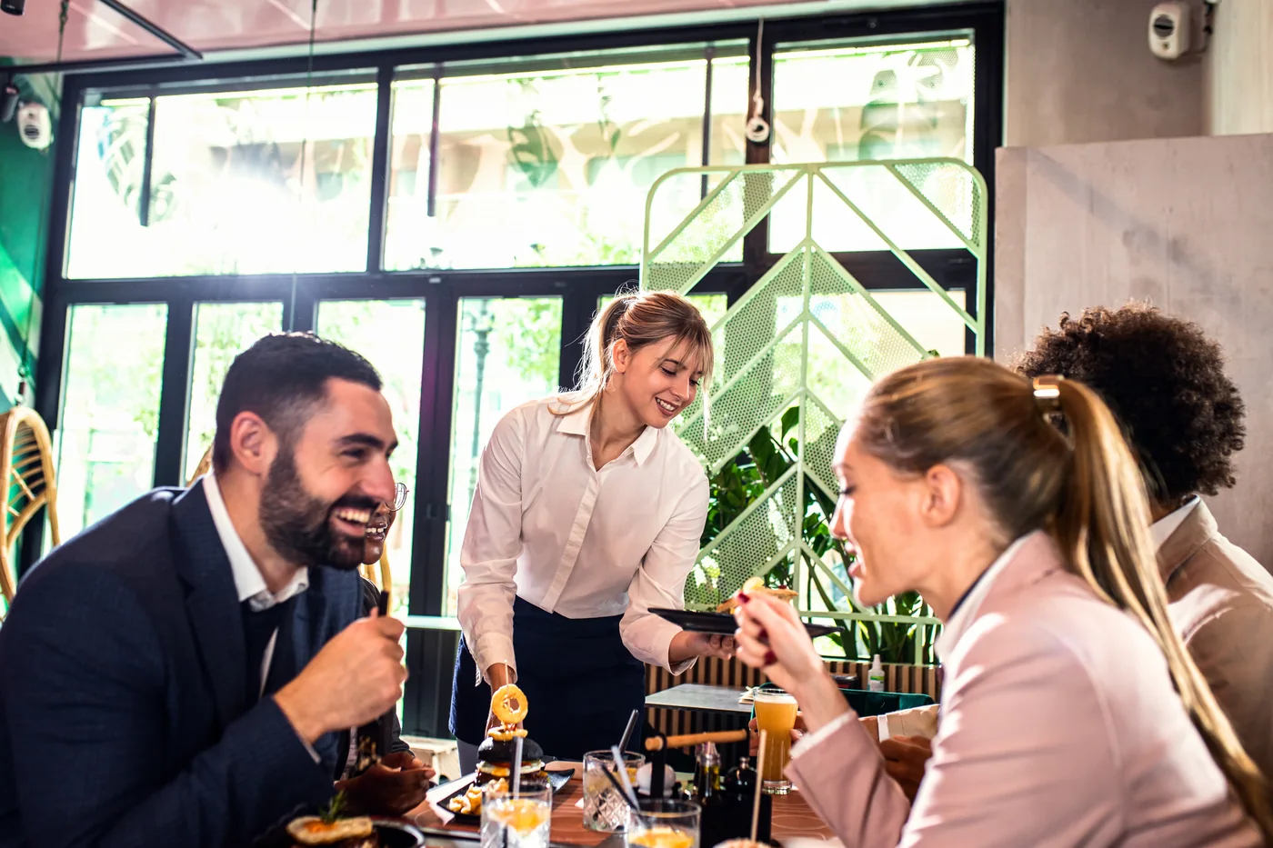 Server delivering drinks to guests at a busy restaurant table.