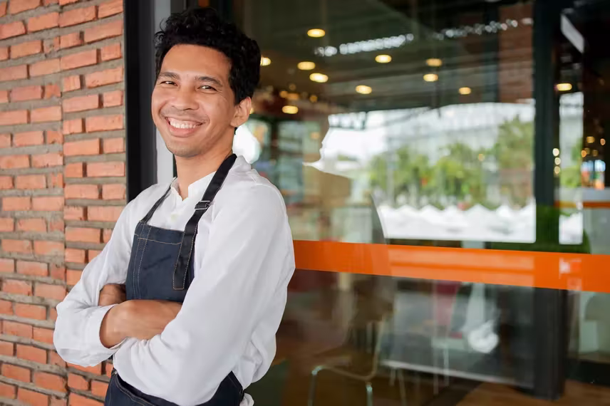 Smiling server in an apron outside a restaurant window.