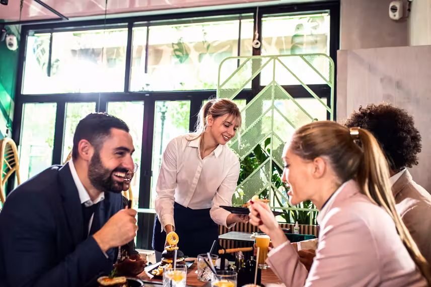 Server delivering drinks to guests at a busy restaurant table.