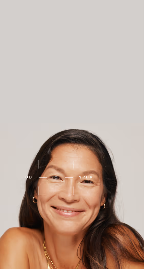Smiling woman with long dark hair and gold earrings and necklaces on a plain background.