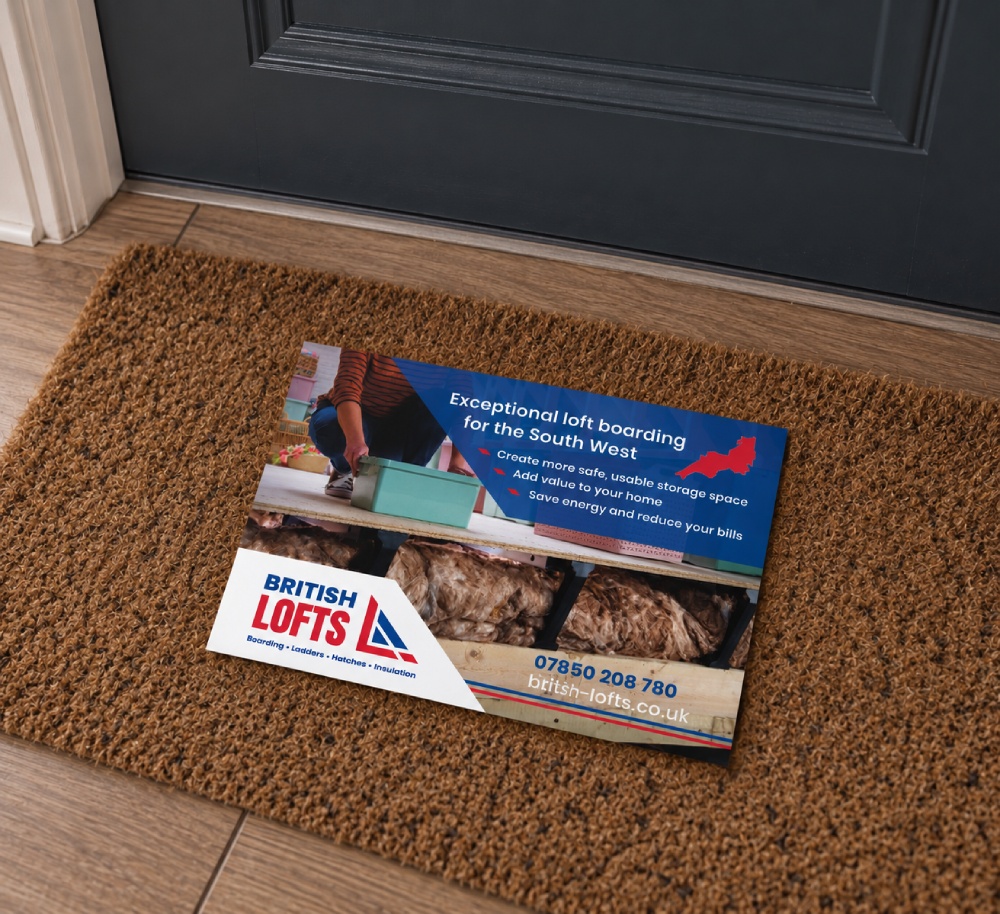 A British Lofts leaflet placed on a brown doormat in front of a dark-colored door, promoting loft boarding services for the South West with benefits like safe storage, home value, and energy savings, including contact number and website.