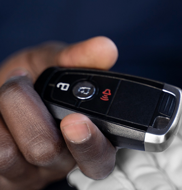 Close-up of a dark-skinned hand holding a black car key fob with lock and alarm buttons.