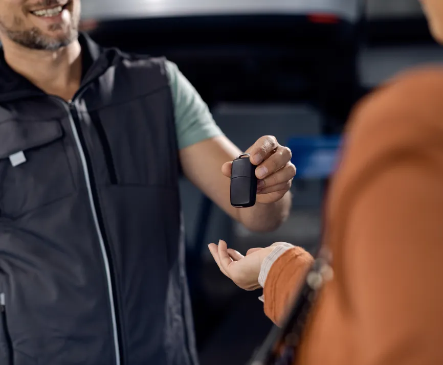 Man smiling while handing a car key fob to another person with an outstretched hand.